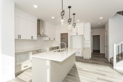 Kitchen with a center island with sink, backsplash, white cabinetry, light wood-type flooring, and light stone counters - 