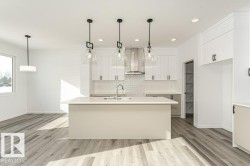 Kitchen featuring white cabinetry, a kitchen island with sink, light wood-style flooring, and hanging light fixtures - 