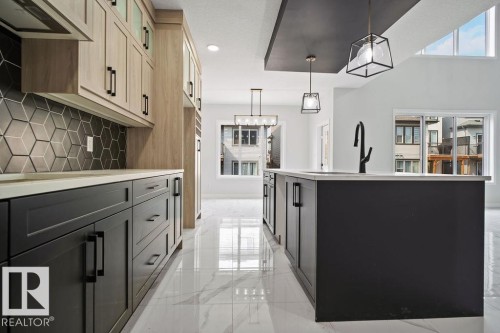 Kitchen featuring extractor fan, a center island with sink, decorative light fixtures, light marble finish floors, and two tone cabinetry - 3912 41 Avenue, Beaumont, AB - Indoor Photo Showing Other Room