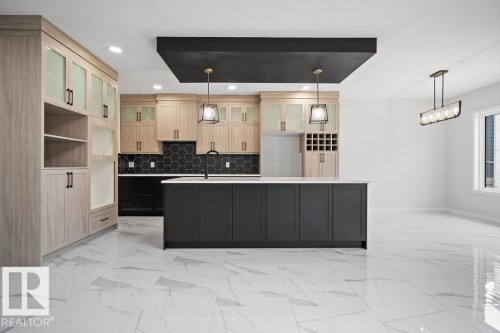 Two tone kitchen featuring dual tone cabinetry, a center island with sink, glass insert cabinets, backsplash, and light marble finish floors - 3912 41 Avenue, Beaumont, AB - Indoor Photo Showing Kitchen