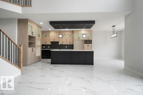 Two tone kitchen with a kitchen island with sink, glass fronted cabinets, open floor plan, two tone cabinets, and light marble finish floors - 3912 41 Avenue, Beaumont, AB - Indoor