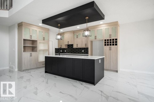 Two tone kitchen with glass fronted cabinets, a center island with sink, two tone cabinetry, light marble finish flooring, and decorative light fixtures - 3912 41 Avenue, Beaumont, AB - Indoor Photo Showing Kitchen