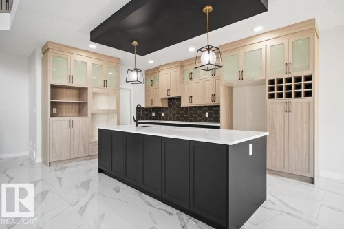 Dual tone kitchen with dual tone cabinets, glass fronted cabinets, a center island with sink, light stone counters, and backsplash - 3912 41 Avenue, Beaumont, AB - Indoor Photo Showing Kitchen