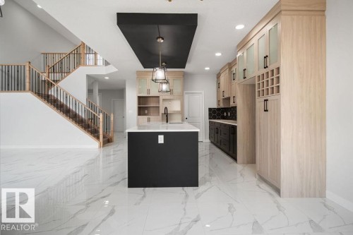Two tone kitchen featuring a center island with sink, dual tone cabinetry, light stone counters, open floor plan, and hanging light fixtures - 3912 41 Avenue, Beaumont, AB - Indoor Photo Showing Kitchen