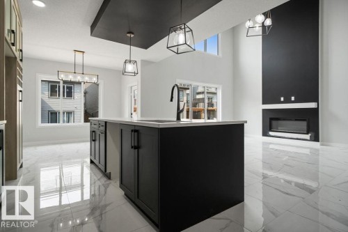 Kitchen featuring dark cabinets, light marble finish floors, a center island with sink, a high ceiling, and hanging lights - 3912 41 Avenue, Beaumont, AB - Indoor