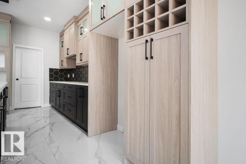 Two tone kitchen featuring glass insert cabinets, two tone cabinetry, light marble finish floors, tasteful backsplash, and light stone counters - 3912 41 Avenue, Beaumont, AB - Indoor