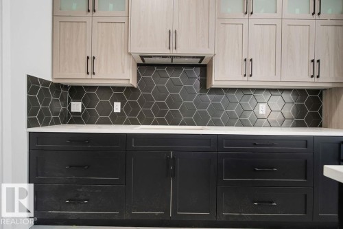 Dual tone kitchen with glass insert cabinets, two tone color scheme, light stone countertops, decorative backsplash, and stovetop - 3912 41 Avenue, Beaumont, AB - Indoor