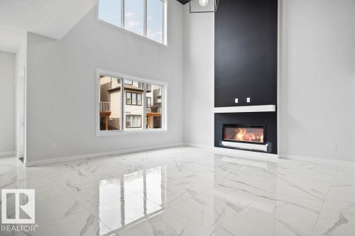 Unfurnished living room featuring light marble finish flooring, a high ceiling, and a glass covered fireplace - 3912 41 Avenue, Beaumont, AB - Indoor With Fireplace