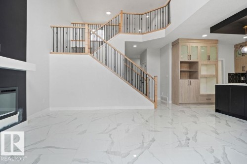 Unfurnished living room with a glass covered fireplace, light marble finish flooring, a high ceiling, and recessed lighting - 3912 41 Avenue, Beaumont, AB - Indoor