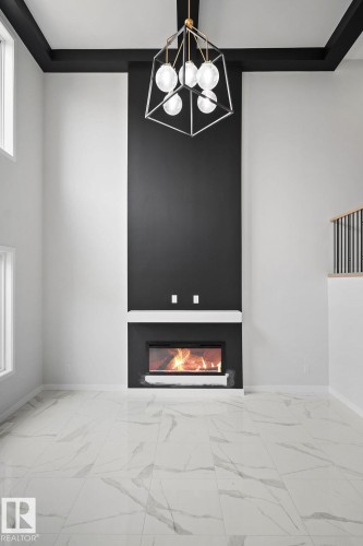 Detailed view of a glass covered fireplace and suspended lighting - 3912 41 Avenue, Beaumont, AB - Indoor Photo Showing Other Room With Fireplace
