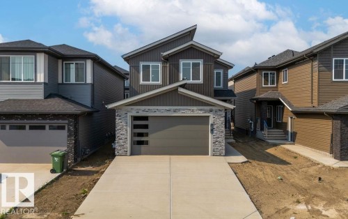 View of front facade with board and batten siding, stone siding, concrete driveway, and an attached garage - 3912 41 Avenue, Beaumont, AB - Outdoor With Facade