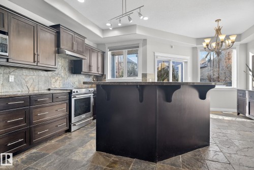 Kitchen with dark wood finish cabinets, stainless steel appliances, a breakfast bar, dark stone countertops, and a kitchen island - 613 Stewart Crescent, Edmonton, AB - Indoor Photo Showing Kitchen With Upgraded Kitchen