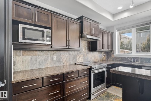 Kitchen with stainless steel appliances, stone finish flooring, dark wood finish cabinets, dark stone counters, and tasteful backsplash - 613 Stewart Crescent, Edmonton, AB - Indoor Photo Showing Kitchen