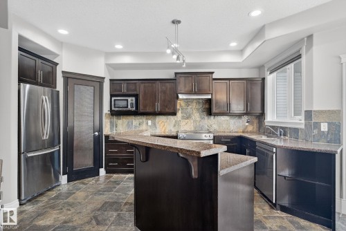 Kitchen featuring dark wood finish cabinets, stainless steel appliances, a breakfast bar area, stone finish floors, and a center island - 613 Stewart Crescent, Edmonton, AB - Indoor Photo Showing Kitchen With Upgraded Kitchen