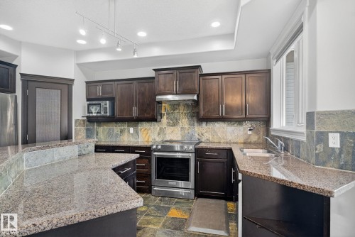 Kitchen featuring stainless steel appliances, dark wood finish cabinets, light stone counters, dark stone finish flooring, and recessed lighting - 613 Stewart Crescent, Edmonton, AB - Indoor Photo Showing Kitchen With Double Sink With Upgraded Kitchen