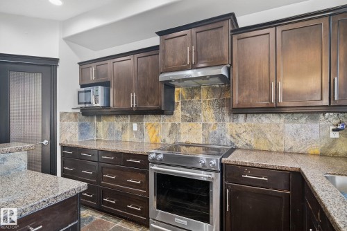 Kitchen featuring stainless steel appliances, dark wood finish cabinets, light stone countertops, dark stone finish flooring, and tasteful backsplash - 613 Stewart Crescent, Edmonton, AB - Indoor Photo Showing Kitchen With Upgraded Kitchen