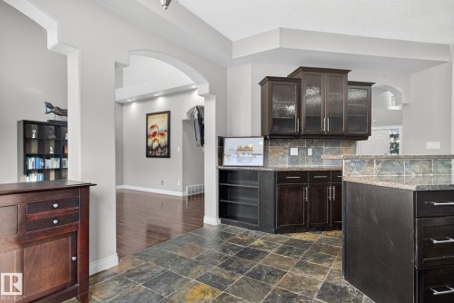 Bar area with arched walkways, dark wood finish cabinets, glass fronted cabinets, and stone tile flooring - 613 Stewart Crescent, Edmonton, AB - Indoor Photo Showing Kitchen