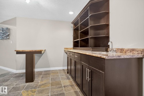 Bar featuring dark wood finish cabinetry, open shelves, stone tile floors, light countertops, and a textured ceiling - 613 Stewart Crescent, Edmonton, AB - Indoor Photo Showing Other Room