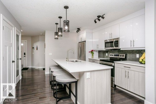 Kitchen with stainless steel appliances, a breakfast bar area, a kitchen island with sink, decorative backsplash, and decorative light fixtures - 6710 Cardinal Road, Edmonton, AB - Indoor Photo Showing Kitchen With Stainless Steel Kitchen With Upgraded Kitchen