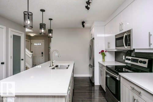 Kitchen with stainless steel appliances, a center island with sink, hanging light fixtures, dark wood-style floors, and white cabinets - 6710 Cardinal Road, Edmonton, AB - Indoor Photo Showing Kitchen With Stainless Steel Kitchen With Double Sink With Upgraded Kitchen