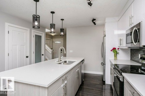 Kitchen featuring stainless steel appliances, an island with sink, decorative light fixtures, light stone countertops, and a textured ceiling - 6710 Cardinal Road, Edmonton, AB - Indoor Photo Showing Kitchen With Double Sink