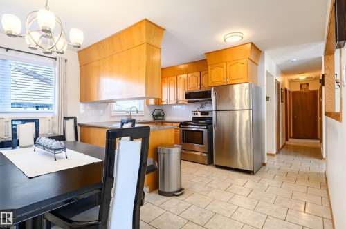 Kitchen with stainless steel appliances, decorative backsplash, light countertops, a chandelier, and light tile patterned floors - 13420 113A St, Edmonton, AB - Indoor Photo Showing Kitchen