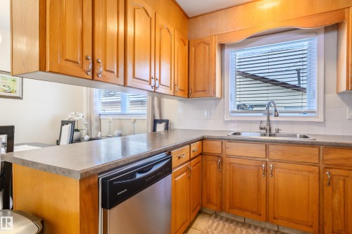 Kitchen with a peninsula, stainless steel dishwasher, wood finish cabinets, and tasteful backsplash - 13420 113A St, Edmonton, AB - Indoor Photo Showing Kitchen With Double Sink