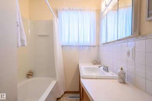 Bathroom featuring vanity, shower / bath combination with curtain, tile walls, and light tile patterned flooring - 13420 113A St, Edmonton, AB - Indoor Photo Showing Bathroom