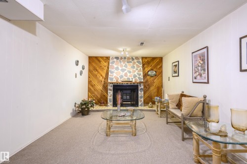 Carpeted living room featuring wood walls and a stone fireplace - 13420 113A St, Edmonton, AB - Indoor Photo Showing Living Room With Fireplace