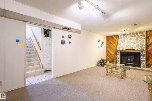 Unfurnished living room featuring wooden walls, carpet, a stone fireplace, rail lighting, and tile patterned flooring - 13420 113A St, Edmonton, AB - Indoor With Fireplace