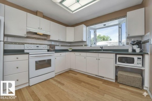 Kitchen featuring white appliances, dark countertops, white cabinetry, light wood finished floors, and decorative backsplash - 4406 39 Ave, Leduc, AB - Indoor Photo Showing Kitchen