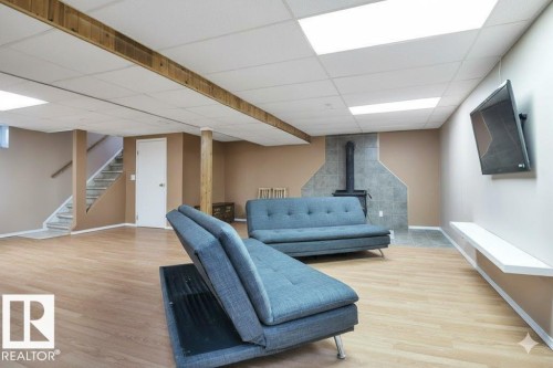 Living room featuring light wood-type flooring, a wood stove, and a drop ceiling - 4406 39 Ave, Leduc, AB - Indoor Photo Showing Basement