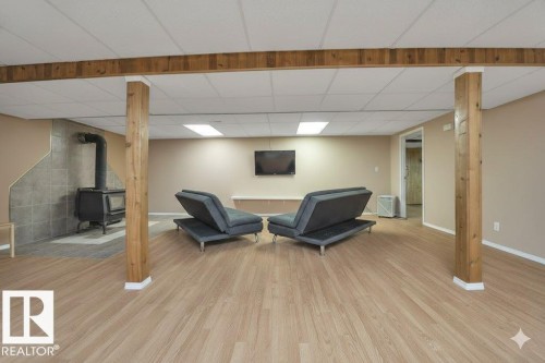 Sitting room featuring light wood-style flooring, a wood stove, and a paneled ceiling - 4406 39 Ave, Leduc, AB - Indoor Photo Showing Basement