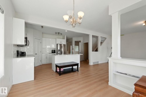 Kitchen with white cabinetry, a center island with sink, light wood-type flooring, stainless steel appliances, and backsplash - 7836 7 Avenue, Edmonton, AB - Indoor Photo Showing Kitchen