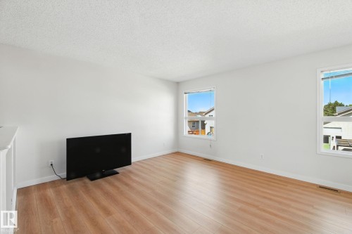 Unfurnished living room featuring a textured ceiling and light wood-style flooring - 7836 7 Avenue, Edmonton, AB - Indoor