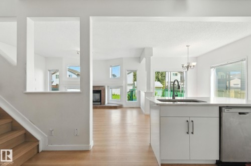 Kitchen featuring stainless steel dishwasher, light wood-style flooring, a tile fireplace, suspended lighting, and white cabinetry - 7836 7 Avenue, Edmonton, AB - Indoor Photo Showing Other Room