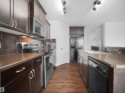 Kitchen featuring dark wood finish cabinets, black appliances, dark countertops, dark wood finished floors, and a center island with sink - 1716 64 Street, Edmonton, AB - Indoor Photo Showing Kitchen With Double Sink