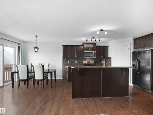 Kitchen with dark wood finish cabinetry, a breakfast bar, stainless steel appliances, a center island with sink, and dark wood-style flooring - 1716 64 Street, Edmonton, AB - Indoor Photo Showing Kitchen