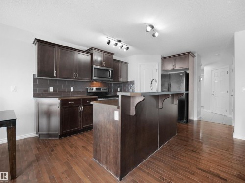 Kitchen featuring a center island with sink, a breakfast bar, stainless steel appliances, dark wood finish cabinets, and decorative backsplash - 1716 64 Street, Edmonton, AB - Indoor Photo Showing Kitchen With Upgraded Kitchen