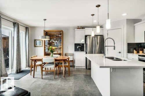 Kitchen with white cabinets, stainless steel appliances, backsplash, an island with sink, and decorative light fixtures - 6485 King Wynd, Edmonton, AB - Indoor Photo Showing Kitchen With Double Sink With Upgraded Kitchen