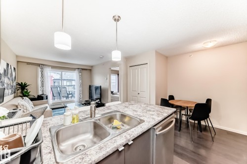 Kitchen with light countertops, open floor plan, dark wood finished floors, stainless steel dishwasher, and decorative light fixtures - 403 340 Windermere Road, Edmonton, AB - Indoor Photo Showing Other Room