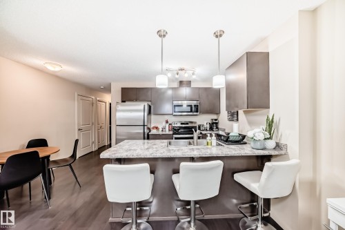 Kitchen featuring a peninsula, a kitchen breakfast bar, stainless steel appliances, pendant lighting, and dark wood finish cabinetry - 403 340 Windermere Road, Edmonton, AB - Indoor