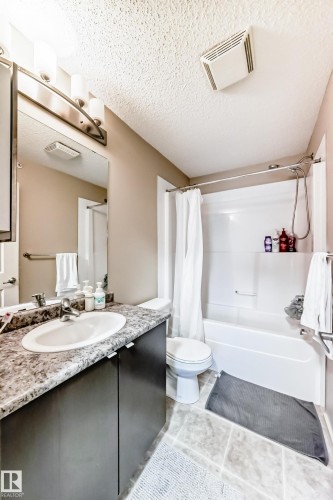 Full bath featuring vanity, shower / bath combination with curtain, a textured ceiling, and light tile patterned floors - 403 340 Windermere Road, Edmonton, AB - Indoor Photo Showing Bathroom