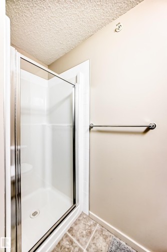 Bathroom with a stall shower, a textured ceiling, and light tile patterned flooring - 403 340 Windermere Road, Edmonton, AB - Indoor Photo Showing Bathroom