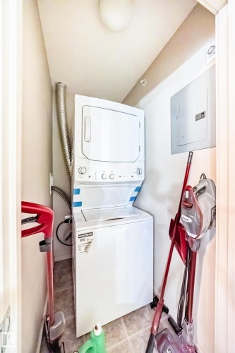 Laundry area featuring electric panel, stacked washer and dryer, and light tile patterned flooring - 403 340 Windermere Road, Edmonton, AB - Indoor Photo Showing Laundry Room