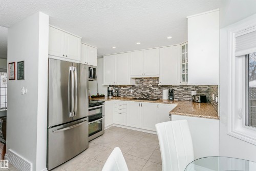 Kitchen with light stone countertops, stainless steel appliances, glass fronted cabinets, light tile patterned floors, and white cabinets - 18507 92 Avenue, Edmonton, AB - Indoor Photo Showing Kitchen With Stainless Steel Kitchen With Upgraded Kitchen