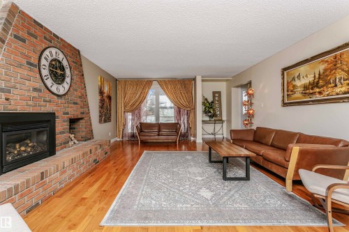 Living area with a textured ceiling, light wood-style flooring, and a brick fireplace - 18507 92 Avenue, Edmonton, AB - Indoor Photo Showing Living Room With Fireplace