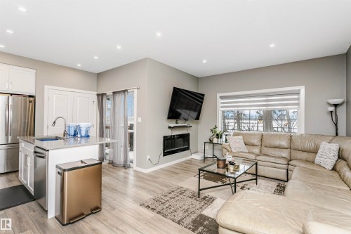 Living room with a glass covered fireplace, light wood-type flooring, recessed lighting, and healthy amount of natural light - 7322 Chivers Crescent, Edmonton, AB - Indoor Photo Showing Living Room