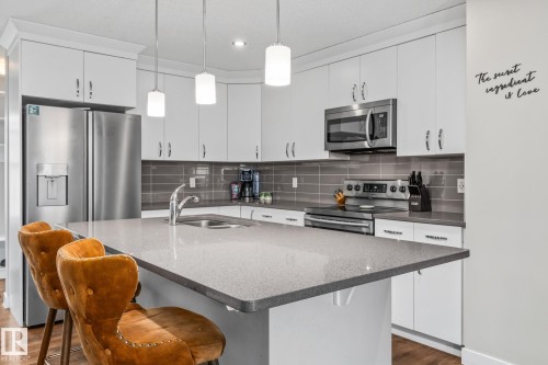 Kitchen featuring stainless steel appliances, white cabinets, dark wood-type flooring, a kitchen breakfast bar, and a kitchen island with sink - 1315 Chappelle Boulevard, Edmonton, AB - Indoor Photo Showing Kitchen With Double Sink With Upgraded Kitchen