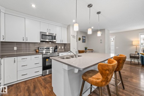 Kitchen featuring stainless steel appliances, decorative backsplash, an island with sink, white cabinetry, and a kitchen bar - 1315 Chappelle Boulevard, Edmonton, AB - Indoor Photo Showing Kitchen With Double Sink With Upgraded Kitchen